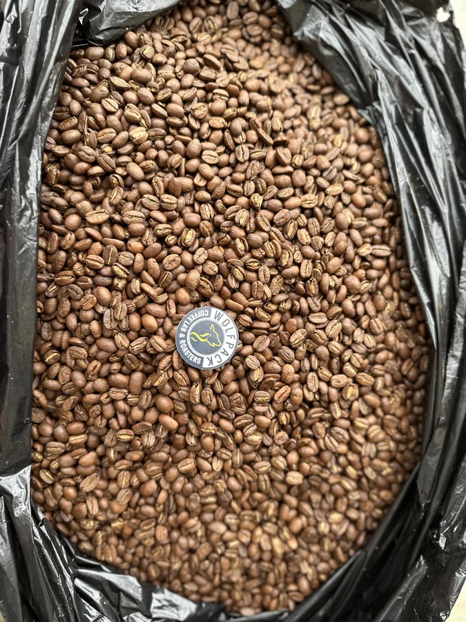 Vista superior de una bolsa abierta con granos de café tostado y el logo circular de Wolfpack