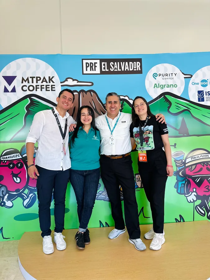 Cuatro colegas posando juntos en el stand de la conferencia PRF El Salvador