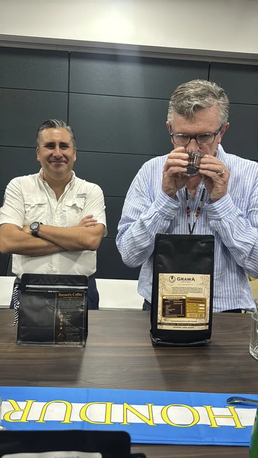 Hombre catando muestras de café en la mesa del panel junto a bandera de Honduras