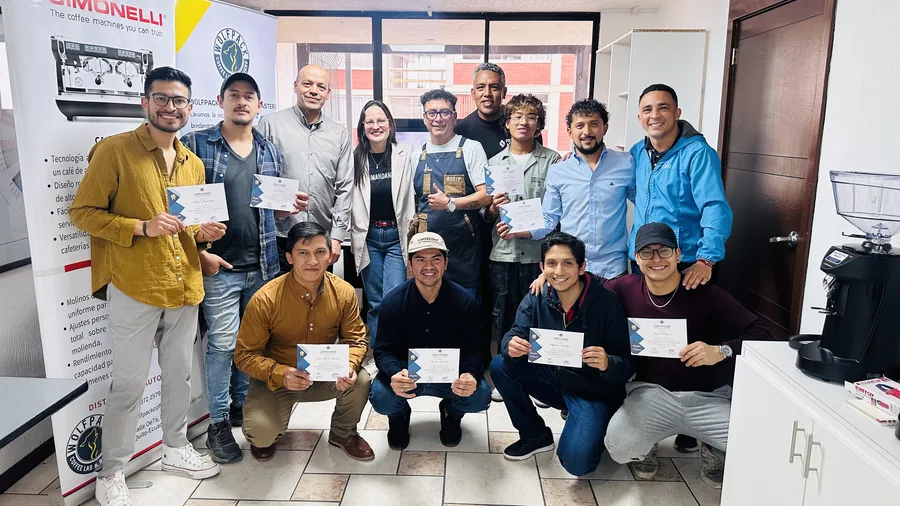 Cohorte completa de estudiantes y staff posando junto al banner de Nuova Simonelli con un certificado