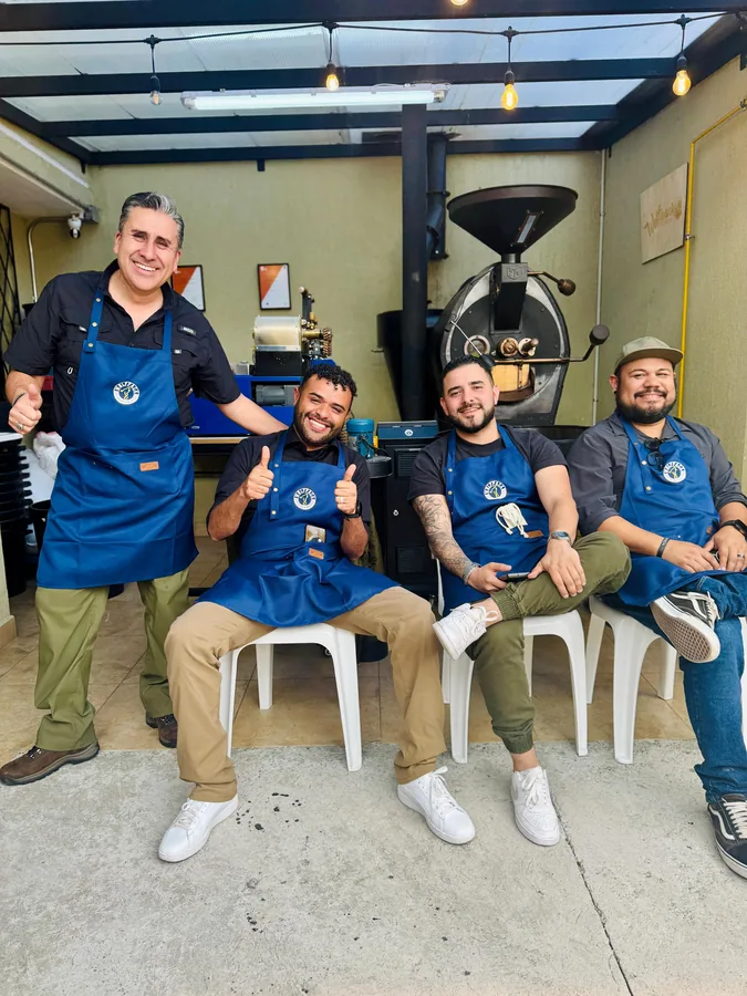 Cuatro tostadores con delantal azul Wolfpack celebrando con pulgares arriba frente a la tostadora