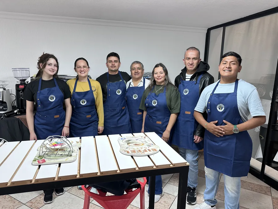 Siete colegas con delantales azules posando juntos alrededor de una mesa baja