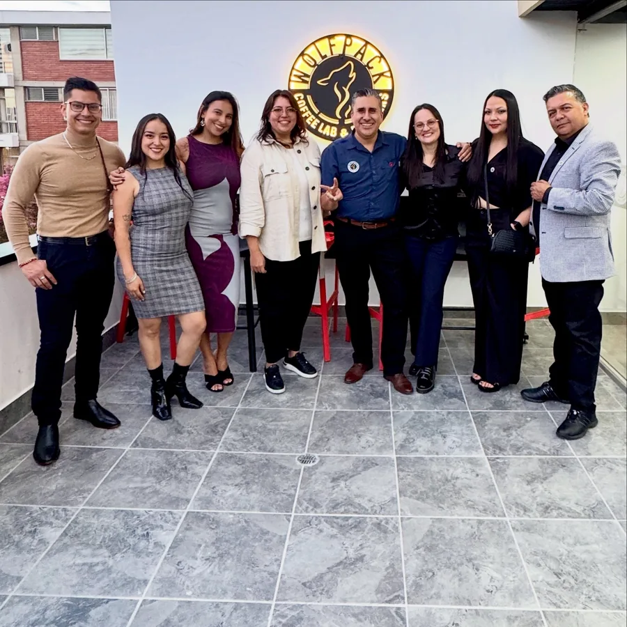 Equipo Wolfpack de ocho personas alineadas en una terraza bajo el letrero iluminado del logo del lobo