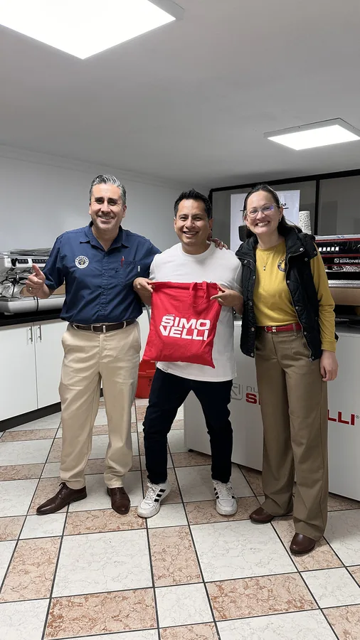 Tres colegas en la oficina sosteniendo una bolsa de regalo de la alianza con Nuova Simonelli