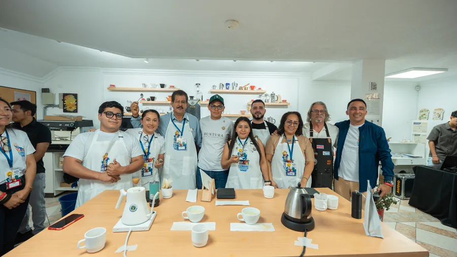 Gran grupo de participantes y staff con lanyards y delantales posando en el laboratorio de café
