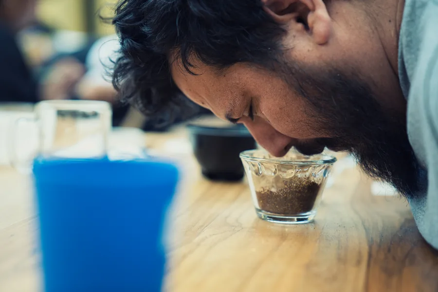 Retrato de perfil de un hombre oliendo café en la mesa de catación, luz dramática