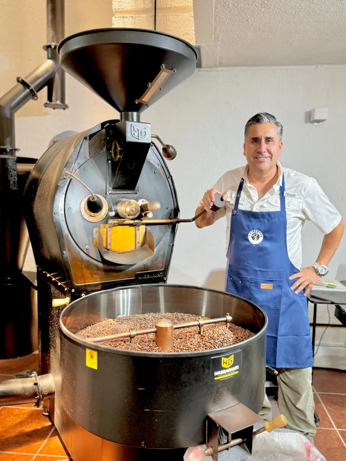 Tostador junto a la máquina industrial con un lote de granos recién tostados en la bandeja